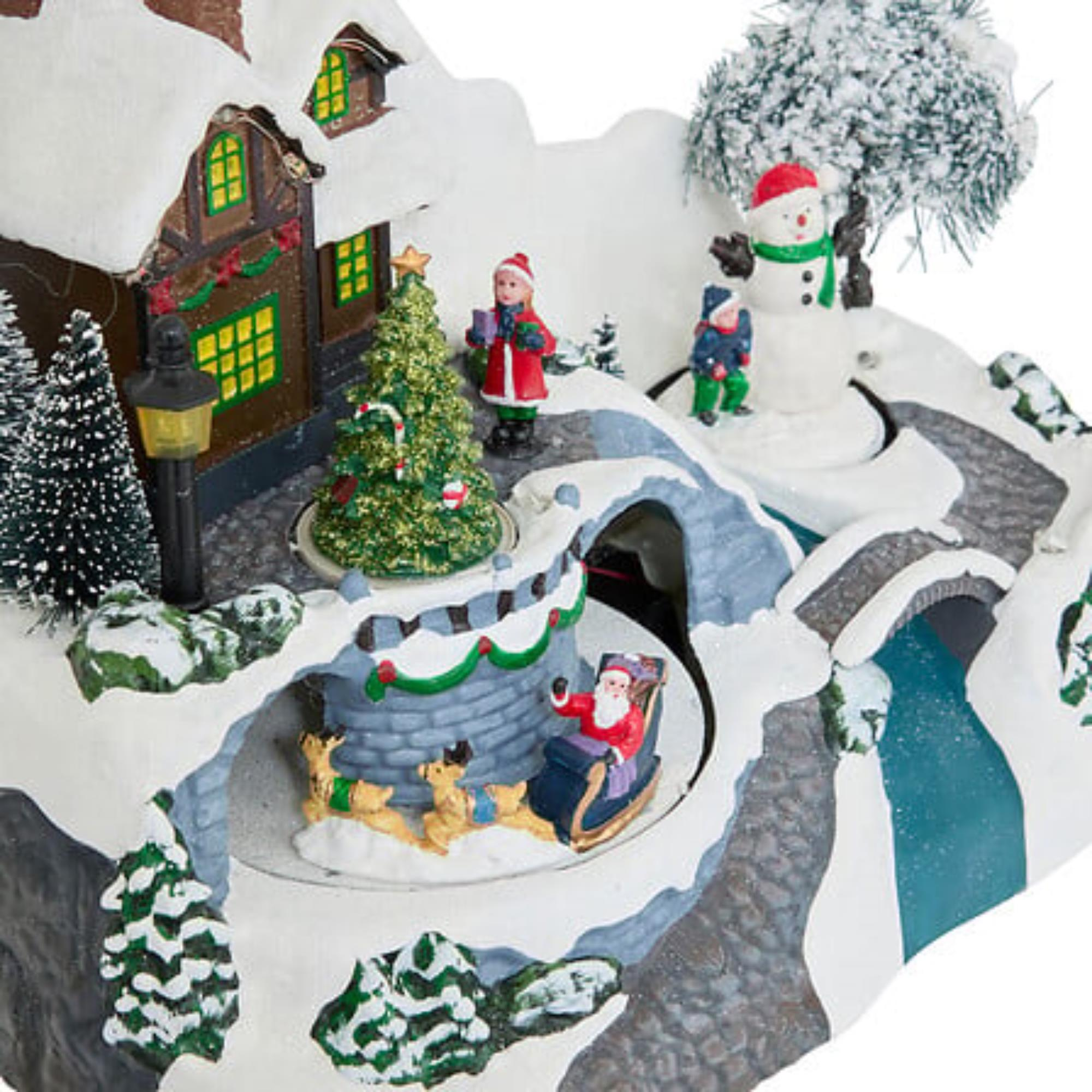 Una escena de un pueblo navideño con Santa en un trineo, un muñeco de nieve, una casa y un puente. La nieve lo cubre todo.