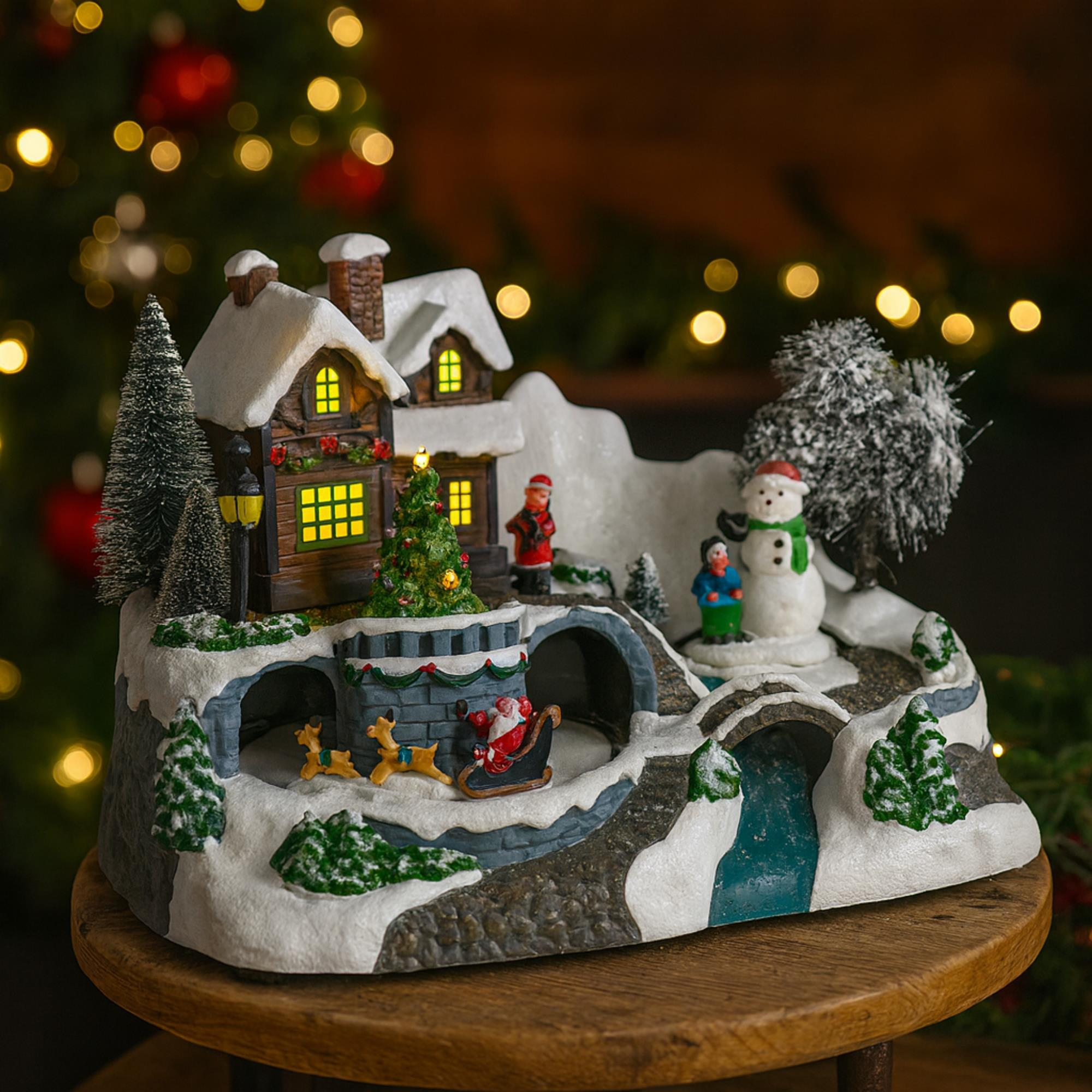 Una escena navideña con el trineo de Papá Noel, un muñeco de nieve, casas, árboles y luces, sobre una mesa de madera.