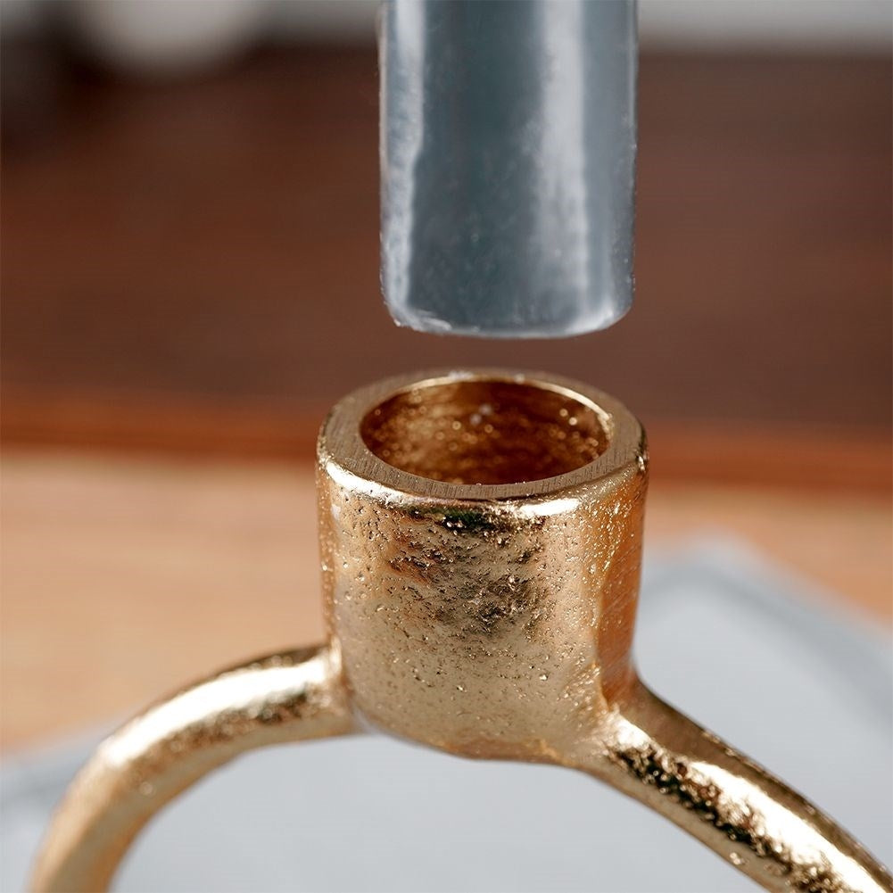Un candelero dorado con una vela gris encima. El soporte tiene una abertura redonda. El fondo es de madera borrosa.