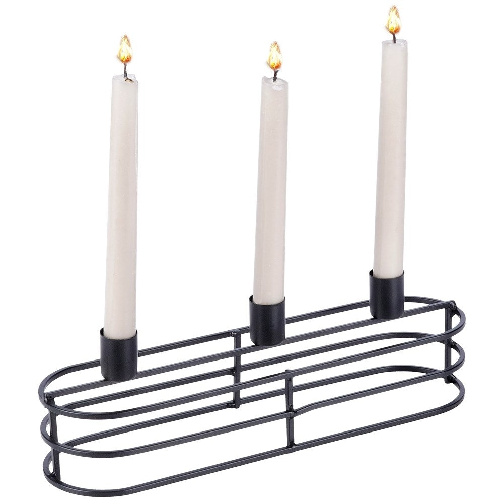 Tres velas encendidas en un portavelas metálico negro. Las velas son blancas y las llamas amarillas. El portavelas es ovalado.