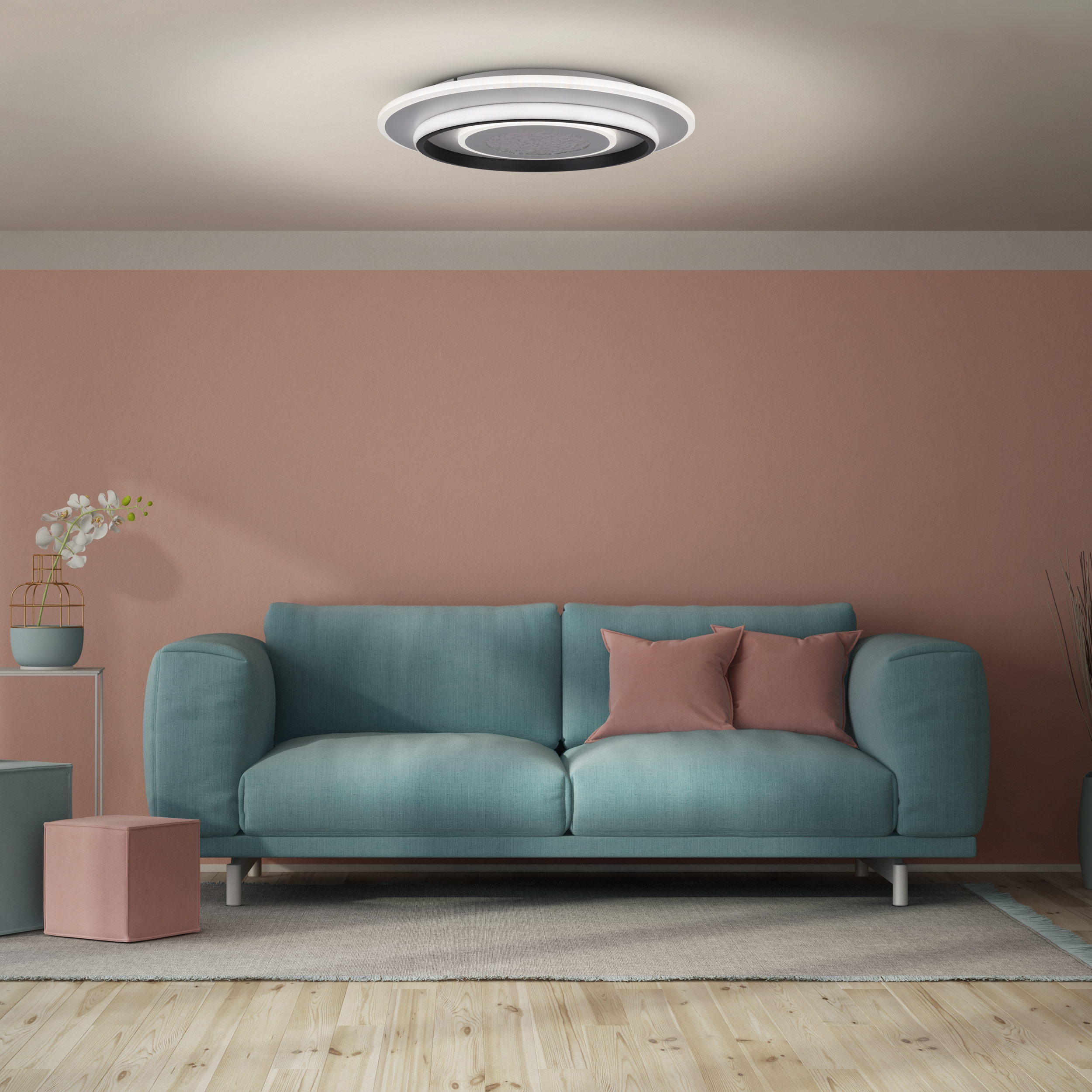 Ein türkisfarbenes Sofa mit rosa Kissen steht vor einer lachsfarbenen Wand. Eine Deckenleuchte hängt darüber. Holzboden.