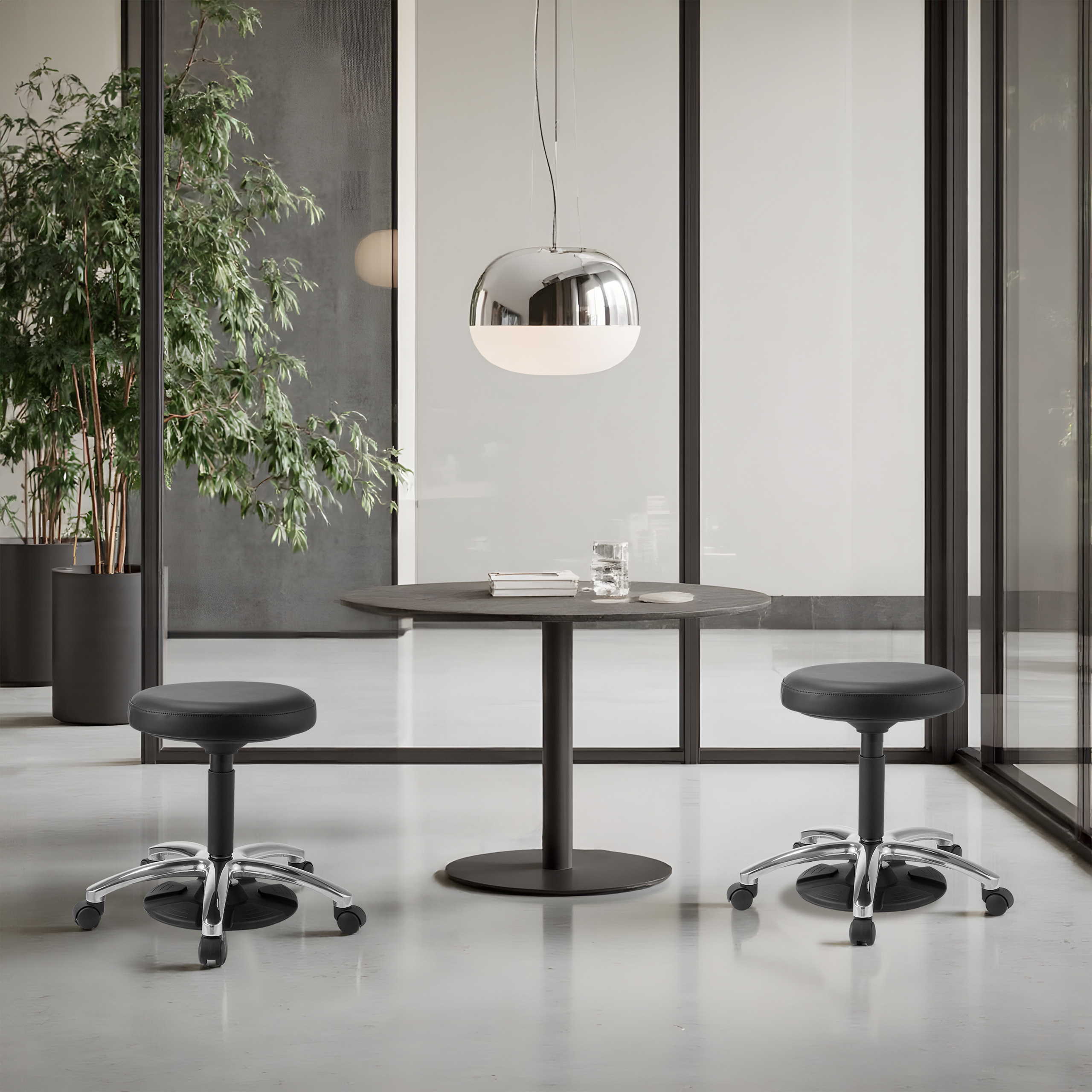 Eine Büroszene mit Tisch, zwei Hockern und einer Pflanze. Über dem Tisch hängt eine moderne Lampe.