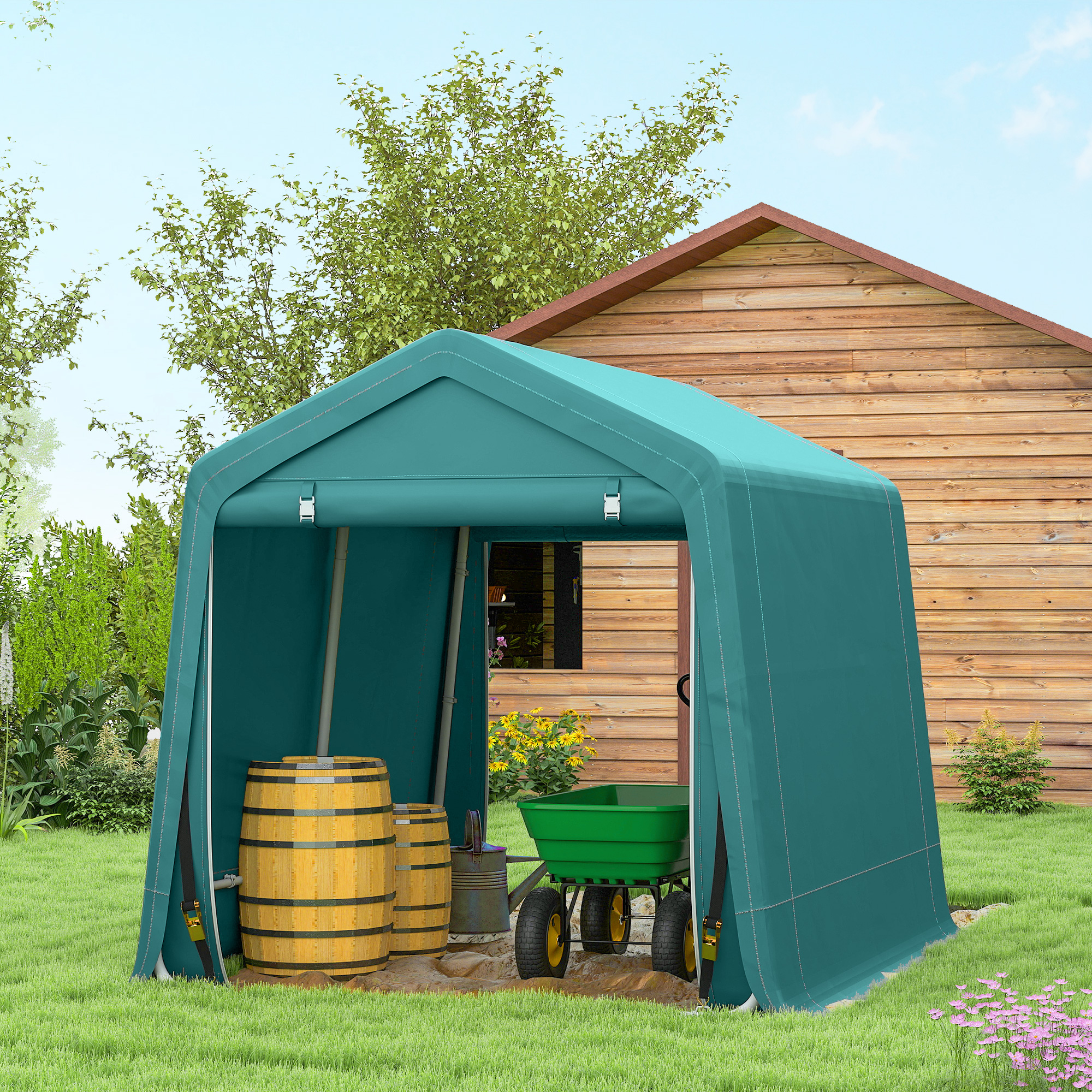 Un capannone verde acqua con botti di legno e un carrello verde si trova sull'erba, con una casa di legno sullo sfondo.