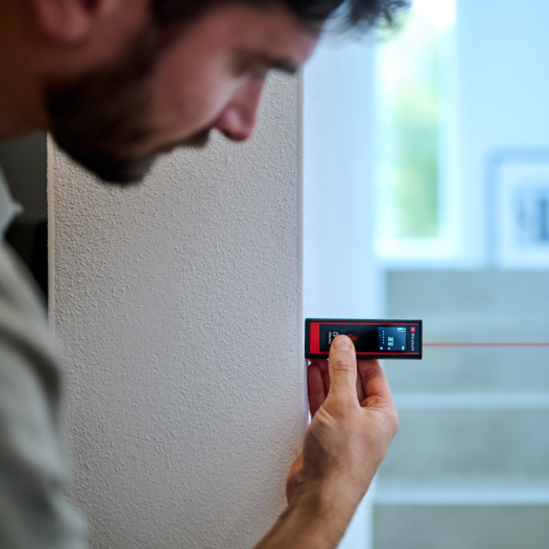 Un uomo usa un telemetro laser su un muro. Il dispositivo proietta una linea rossa. Lo sfondo è sfocato.