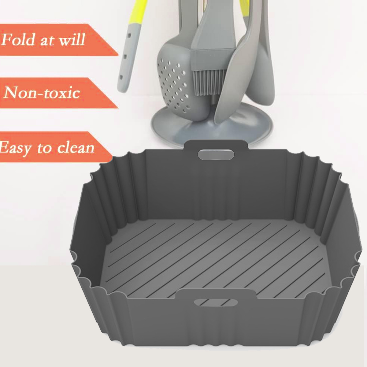 Ein grauer Silikon-Airfryer-Korb. Küchenutensilien stehen dahinter. Text: Nach Belieben falten, ungiftig, leicht zu reinigen.