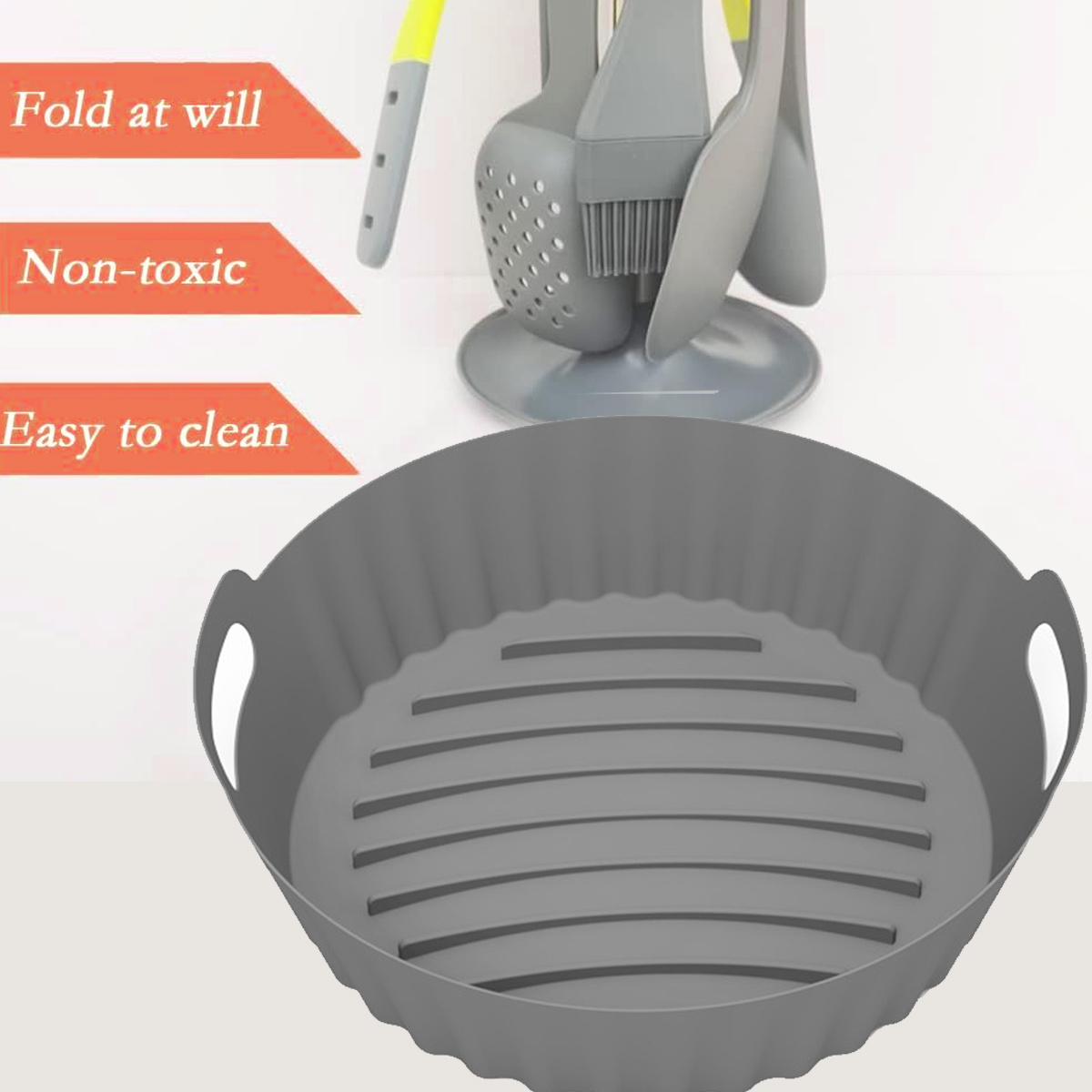 Ein grauer Silikon-Airfryer-Korb mit Griffen. Dahinter stehen Küchenutensilien. Der Text weist darauf hin, dass es ungiftig und leicht zu reinigen ist.