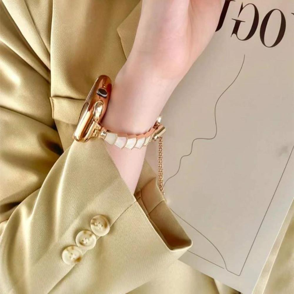 Eine Hand, die eine goldene Uhr und ein Armband trägt, ruht auf einem beigen Blazer. Im Hintergrund befindet sich eine Zeitschrift.