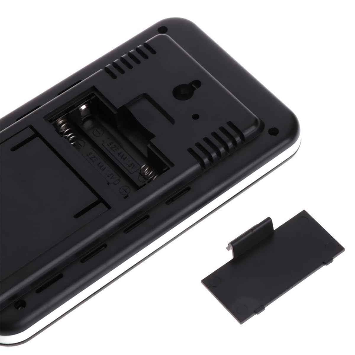 Rückseite eines schwarzen elektronischen Geräts mit offenem Batteriefach. Zwei Batterien sind sichtbar. Eine abgetrennte Abdeckung liegt rechts.