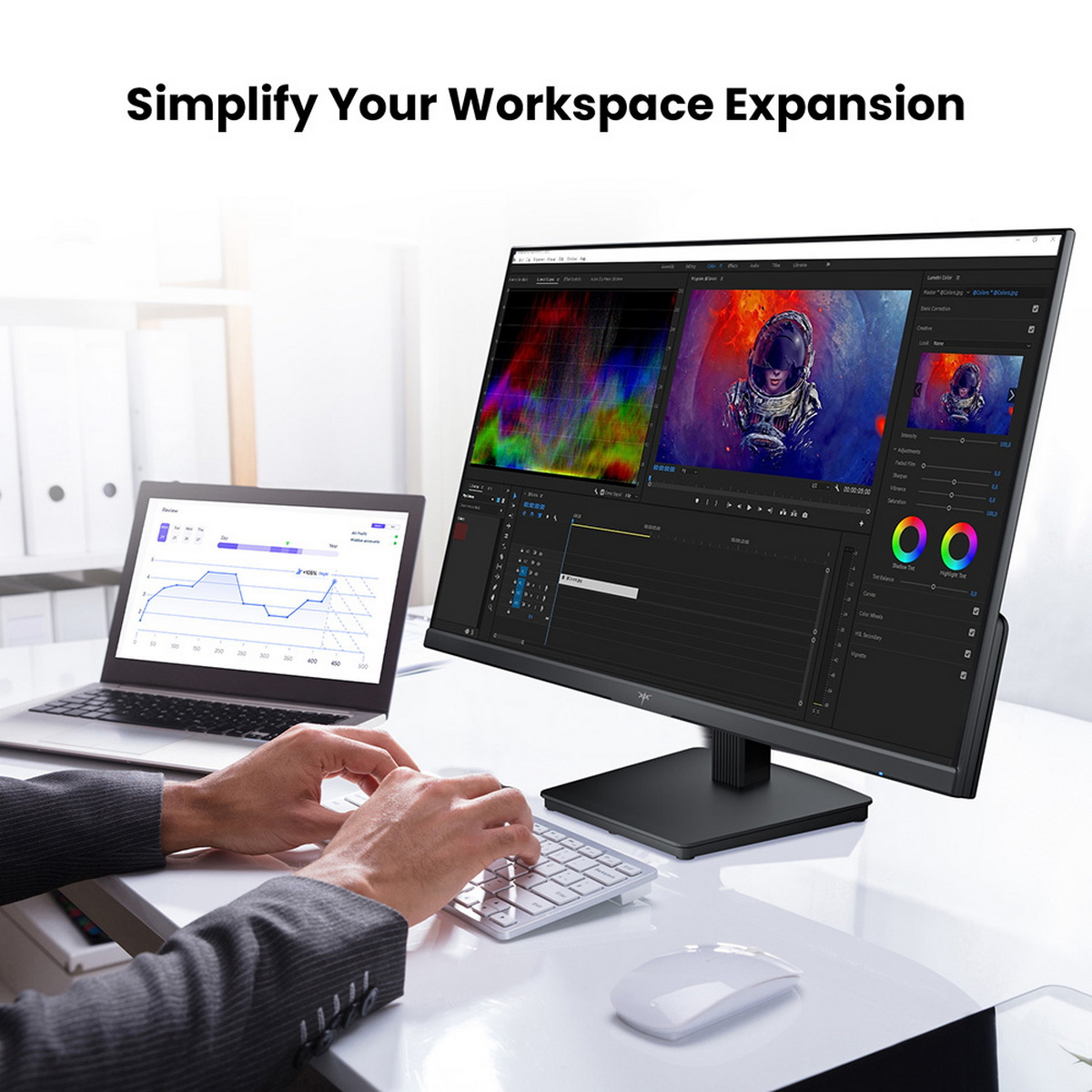 Eine Person tippt auf einer Tastatur. Ein großer Monitor zeigt Videobearbeitungssoftware. Ein Laptop zeigt Diagramme. Weiße Maus auf dem Tisch.