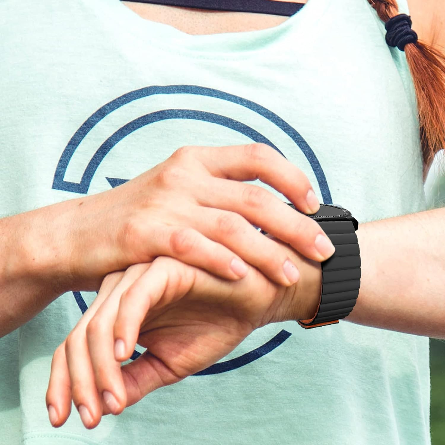 Eine Person, die eine Uhr mit schwarzem Armband trägt, schaut auf die Uhrzeit. Sie trägt ein hellgrünes Hemd. Geflochtenes Haar ist sichtbar.