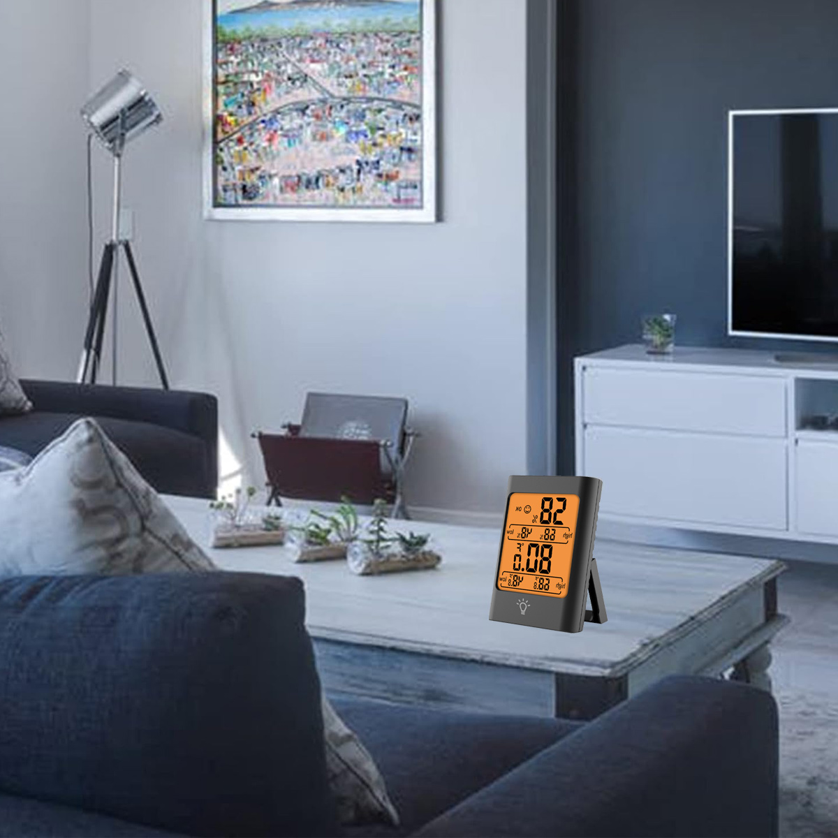 Ein modernes Wohnzimmer mit einem digitalen Thermometer auf einem Tisch. Ein Gemälde hängt an der Wand, und ein Sofa ist im Vordergrund.