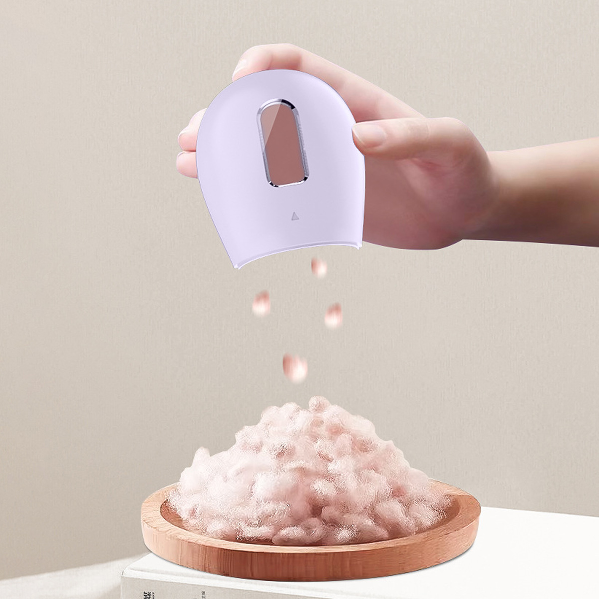 Eine Hand hält ein lavendelfarbenes Gerät, das rosa, flauschiges Material auf einen Holz-Teller mit einem großen Haufen desselben Materials abgibt.