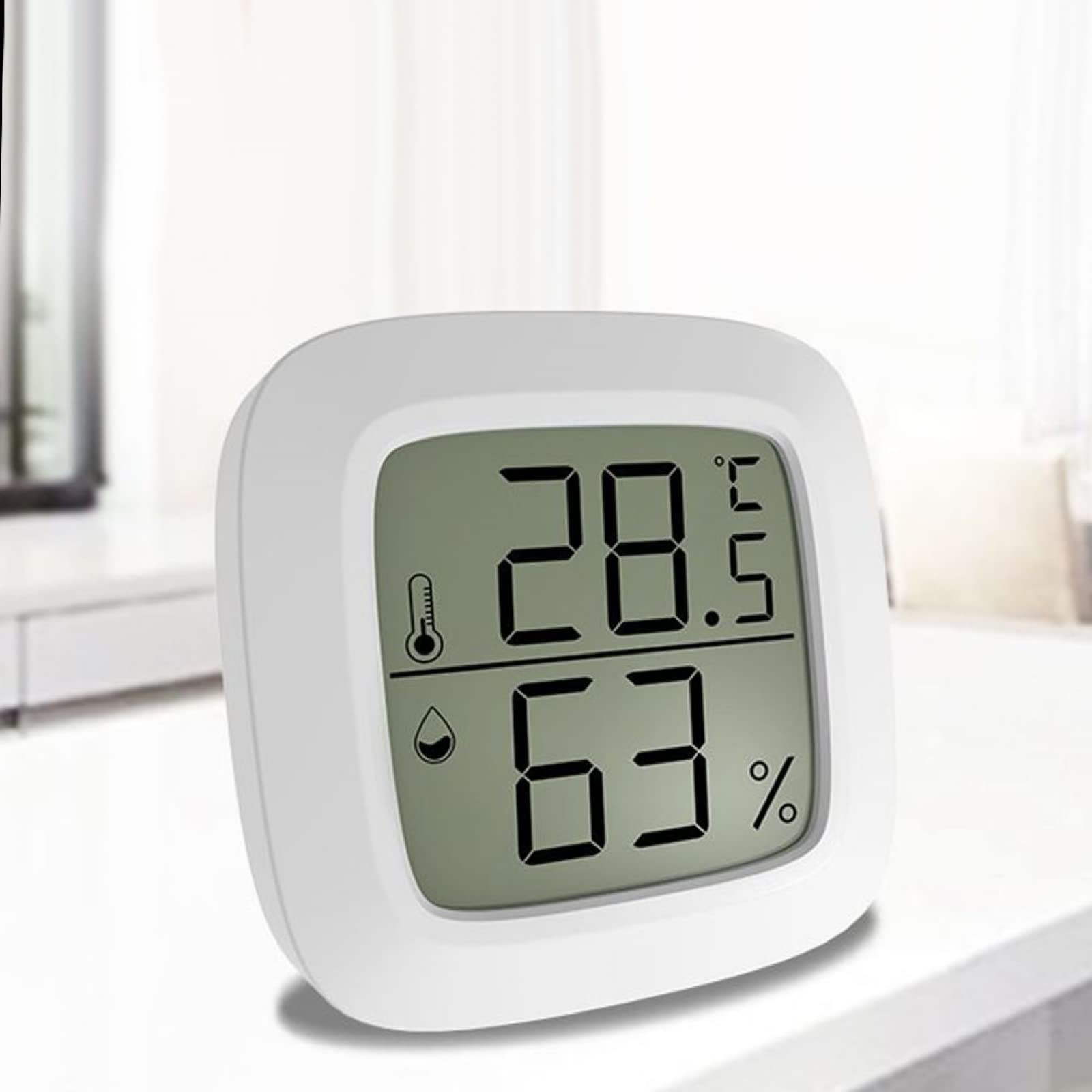 Ein weißes digitales Thermometer zeigt 28,5 °C und 63 % Luftfeuchtigkeit an. Es steht auf einer weißen Oberfläche.