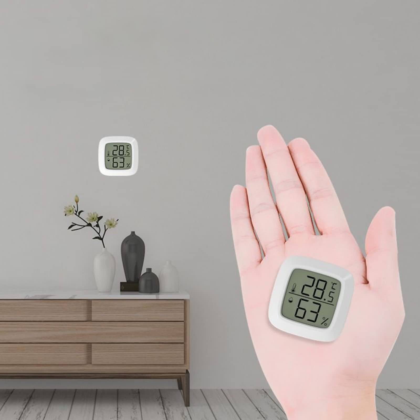 Eine Hand hält ein digitales Thermometer. Ein anderes befindet sich an der Wand. Im Hintergrund ein Schrank mit Vasen und Blumen.