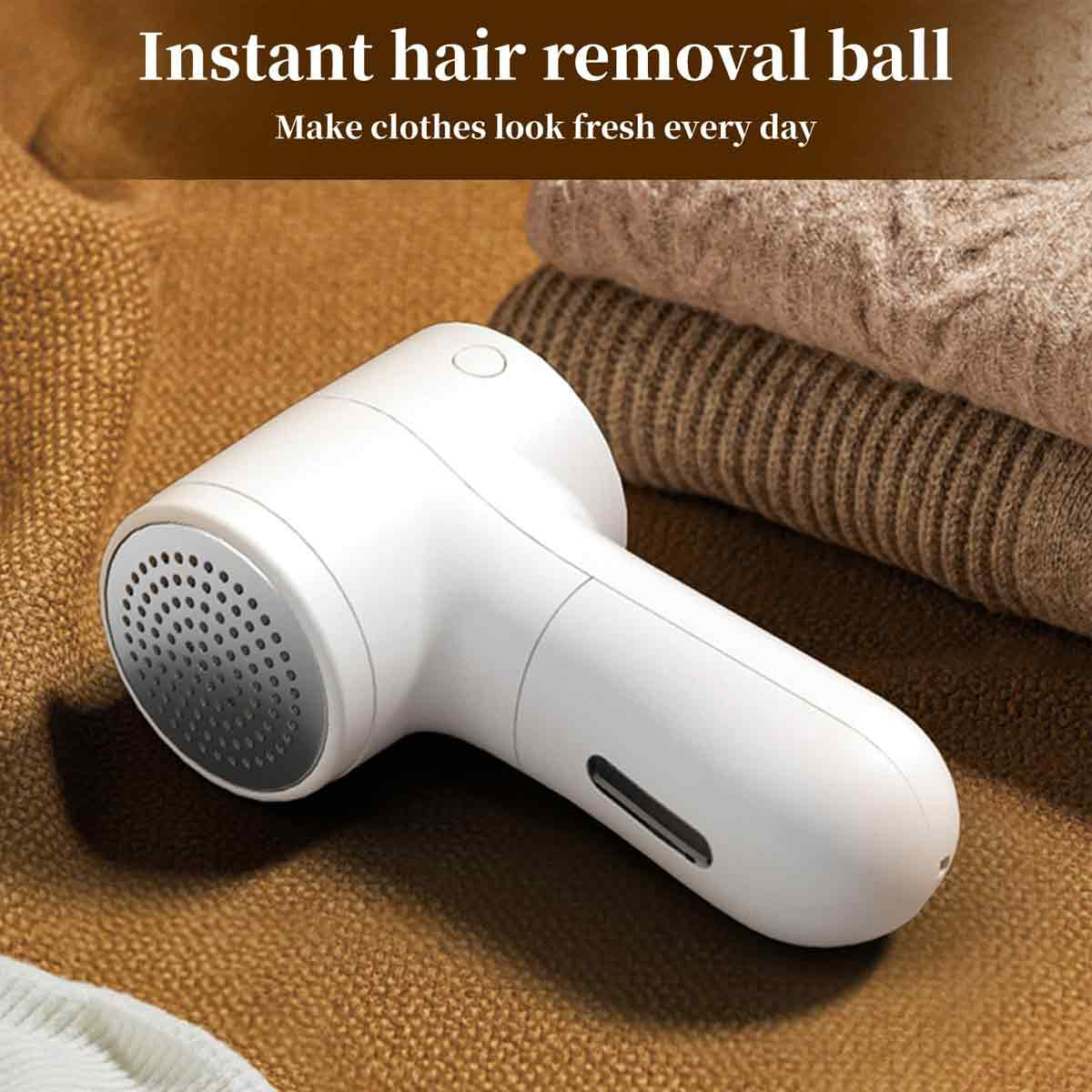 Ein weißer Haar-Entfernungsball liegt auf einer braunen Oberfläche neben gefalteter Kleidung. Das Gerät dient dazu, Kleidung frisch aussehen zu lassen.