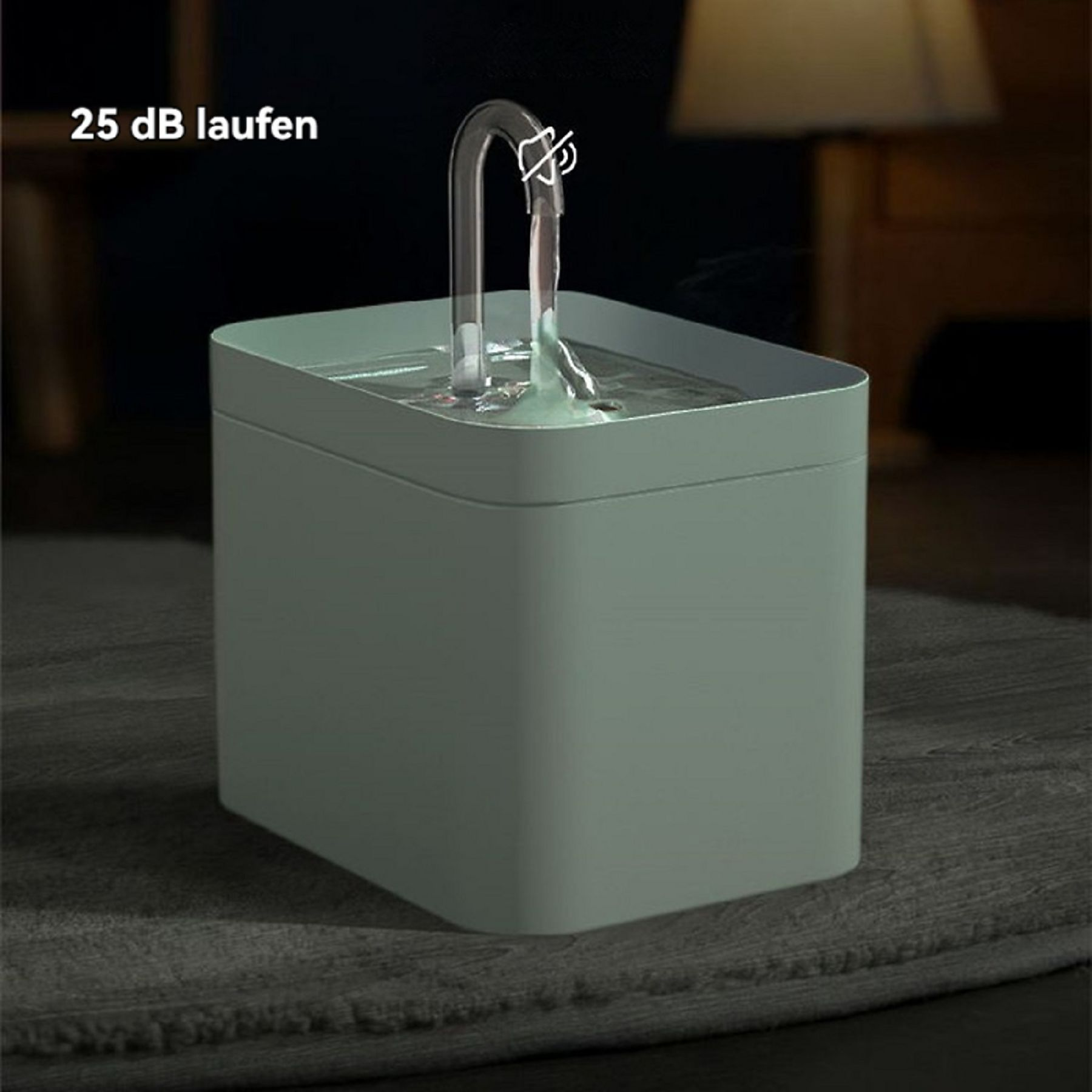 Ein grüner Haustier-Wasserbrunnen, Wasser fließt aus einem durchsichtigen Ausguss. Im Hintergrund eine Lampe und dunkle Wand.
