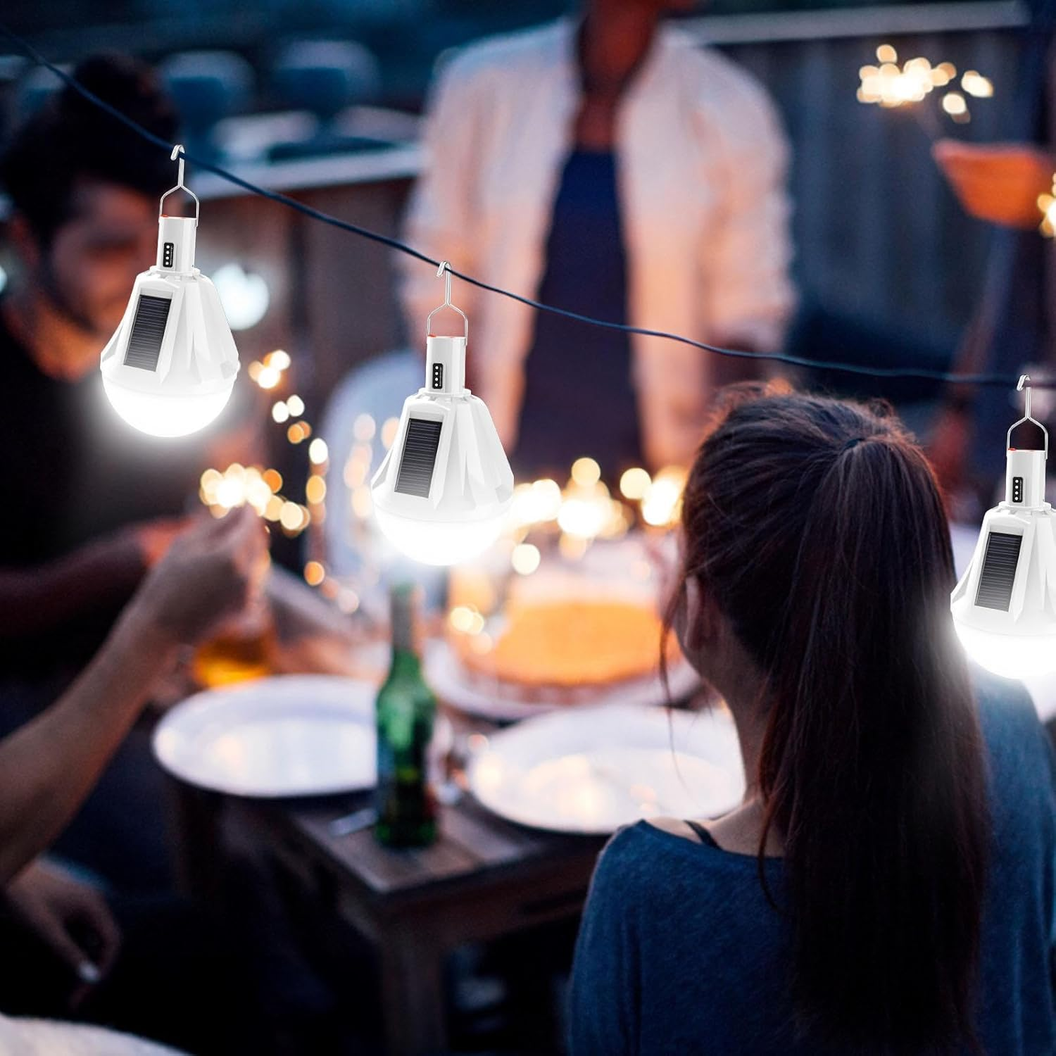 Leute versammelten sich nachts im Freien. Lichterketten, Tische und Essen sind vorhanden. Leute halten Wunderkerzen. Solarleuchten hängen.
