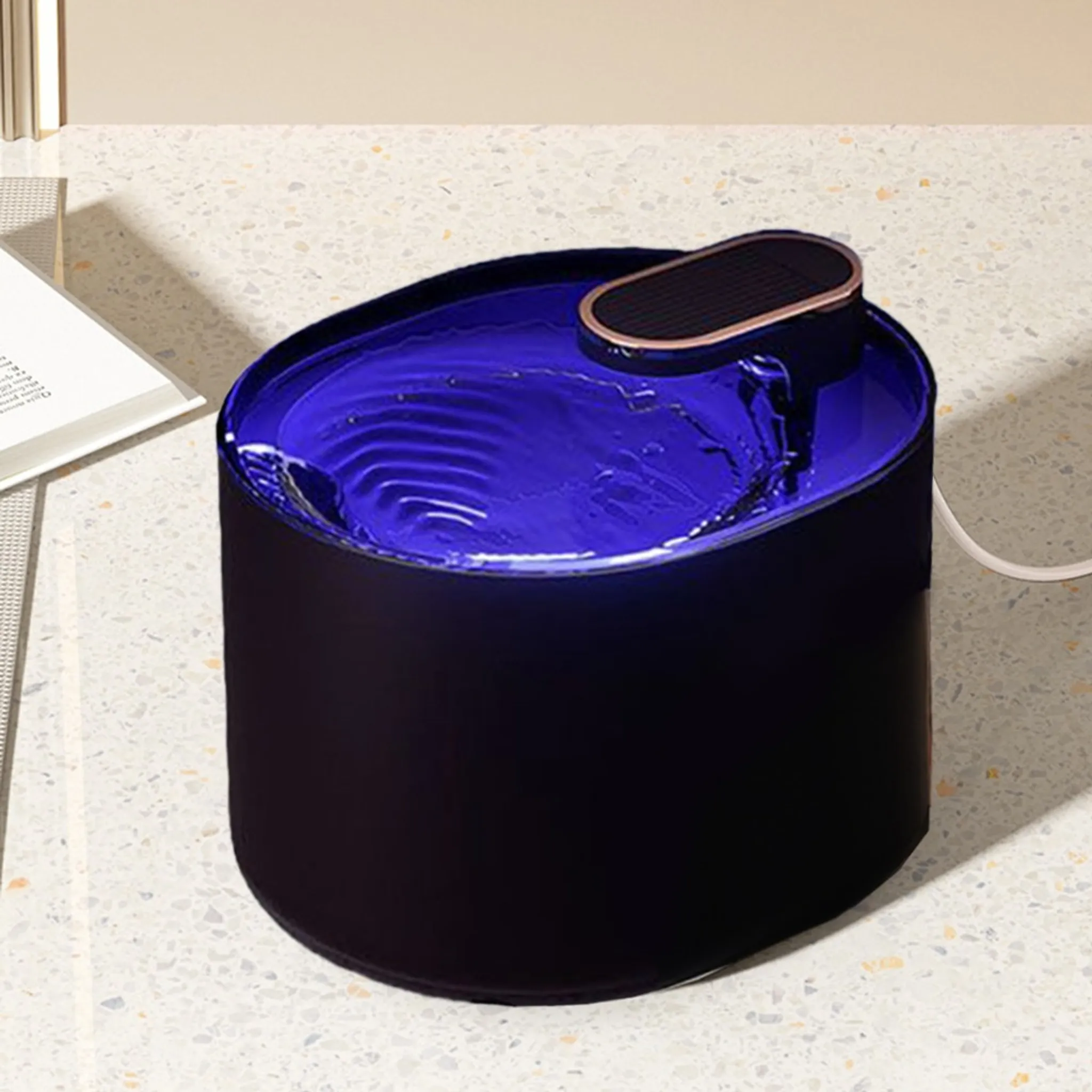 Ein moderner Trinkbrunnen für Haustiere mit blauem Wasser, schwarzer Außenseite und einer kleinen, kupferfarbenen Oberseite.