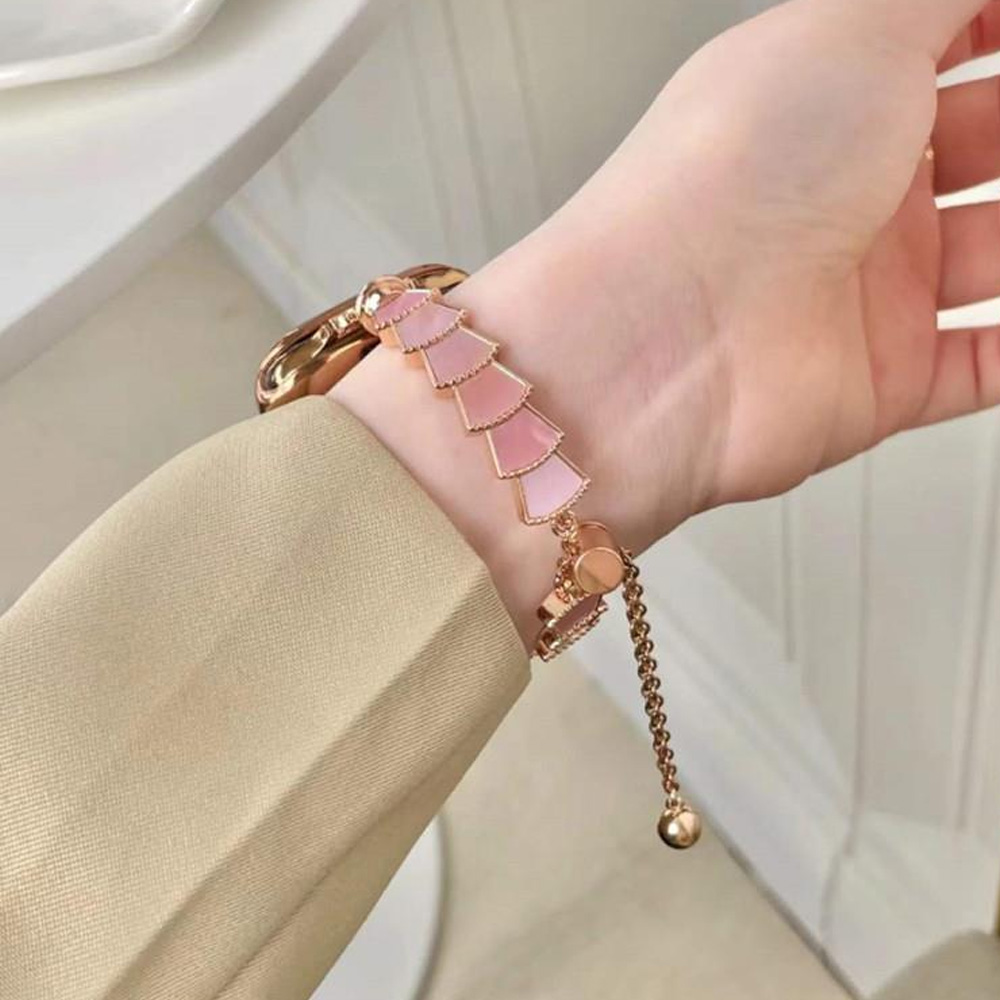 Eine Hand trägt ein roségoldenes Armband mit rosa gestuften Charms. Der Arm ist in einer beigen Jacke. Der Hintergrund ist weiß.