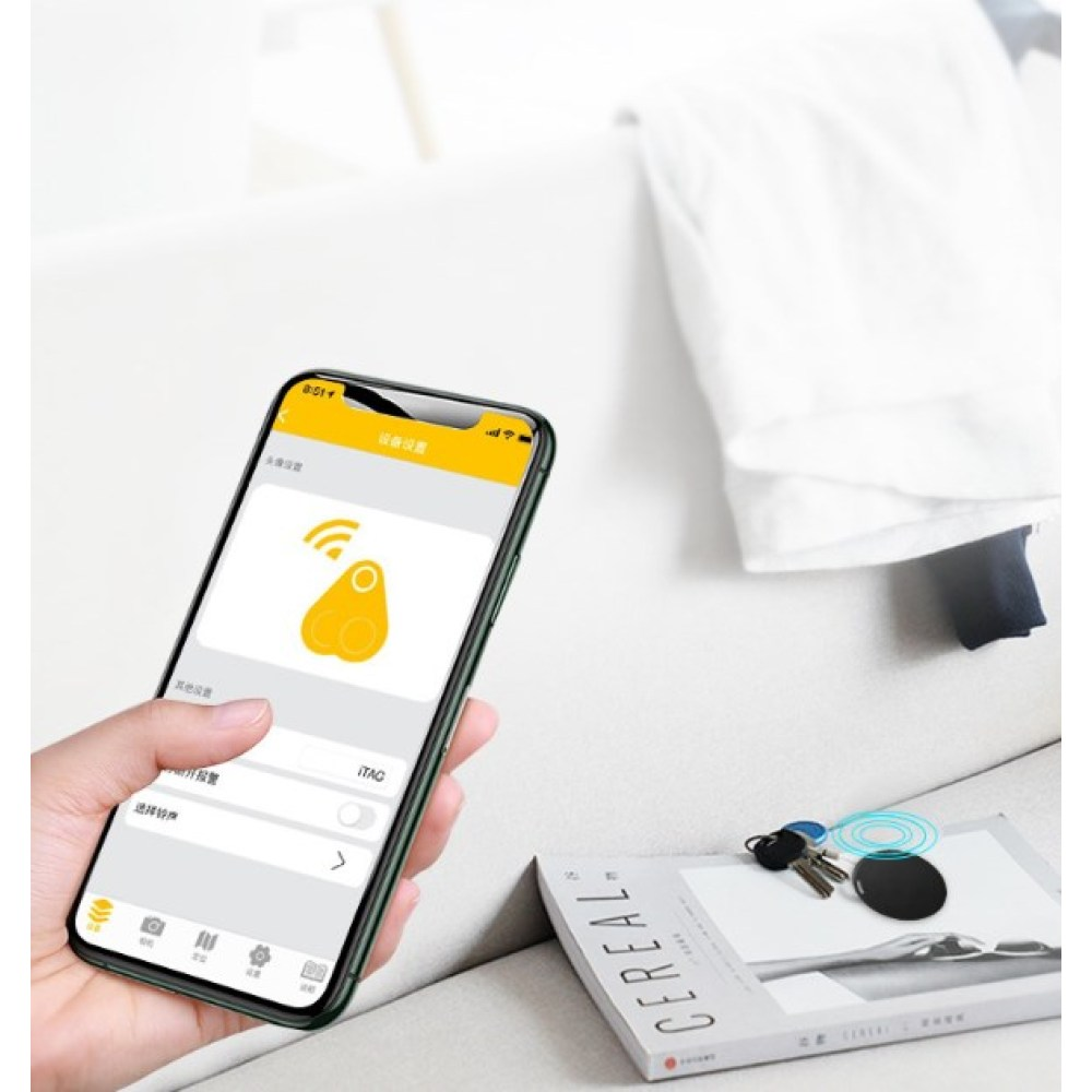 Eine Hand hält ein Telefon, das ein Ortungsgerätsymbol anzeigt. Schlüssel, ein Tracker und eine Müslischachtel liegen auf der Couch. Weißes Hemd im Hintergrund.