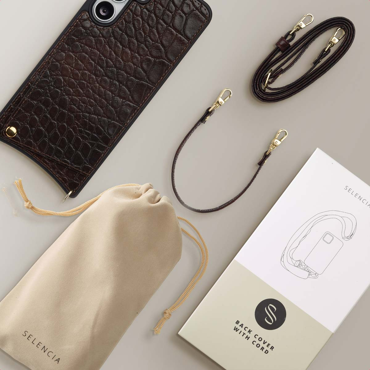 Een telefoonhoesje, leren riem en zakje liggen op een licht oppervlak. Er is ook een doos met een telefoonillustratie en een logo.