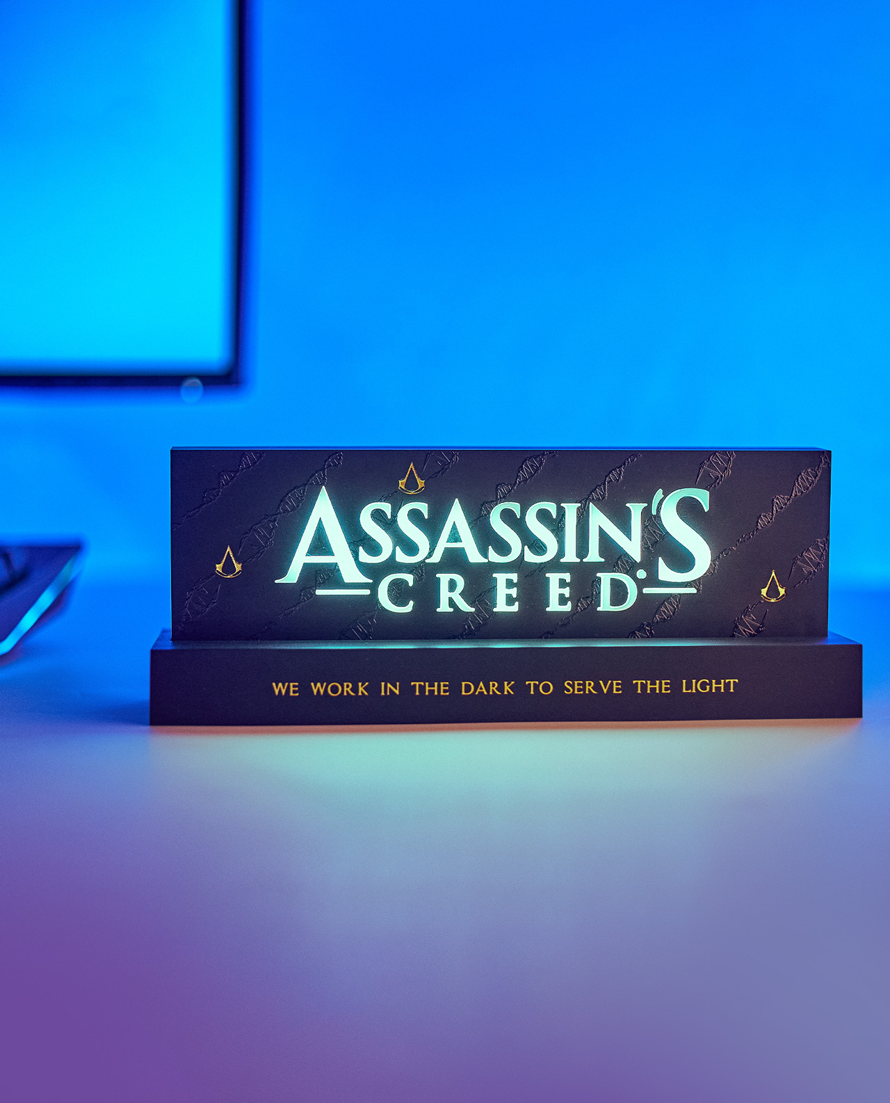 Ein beleuchtetes Assassin's Creed-Schild. Es ist schwarz mit weißer Schrift und einem goldenen Logo. Der Hintergrund ist blau.