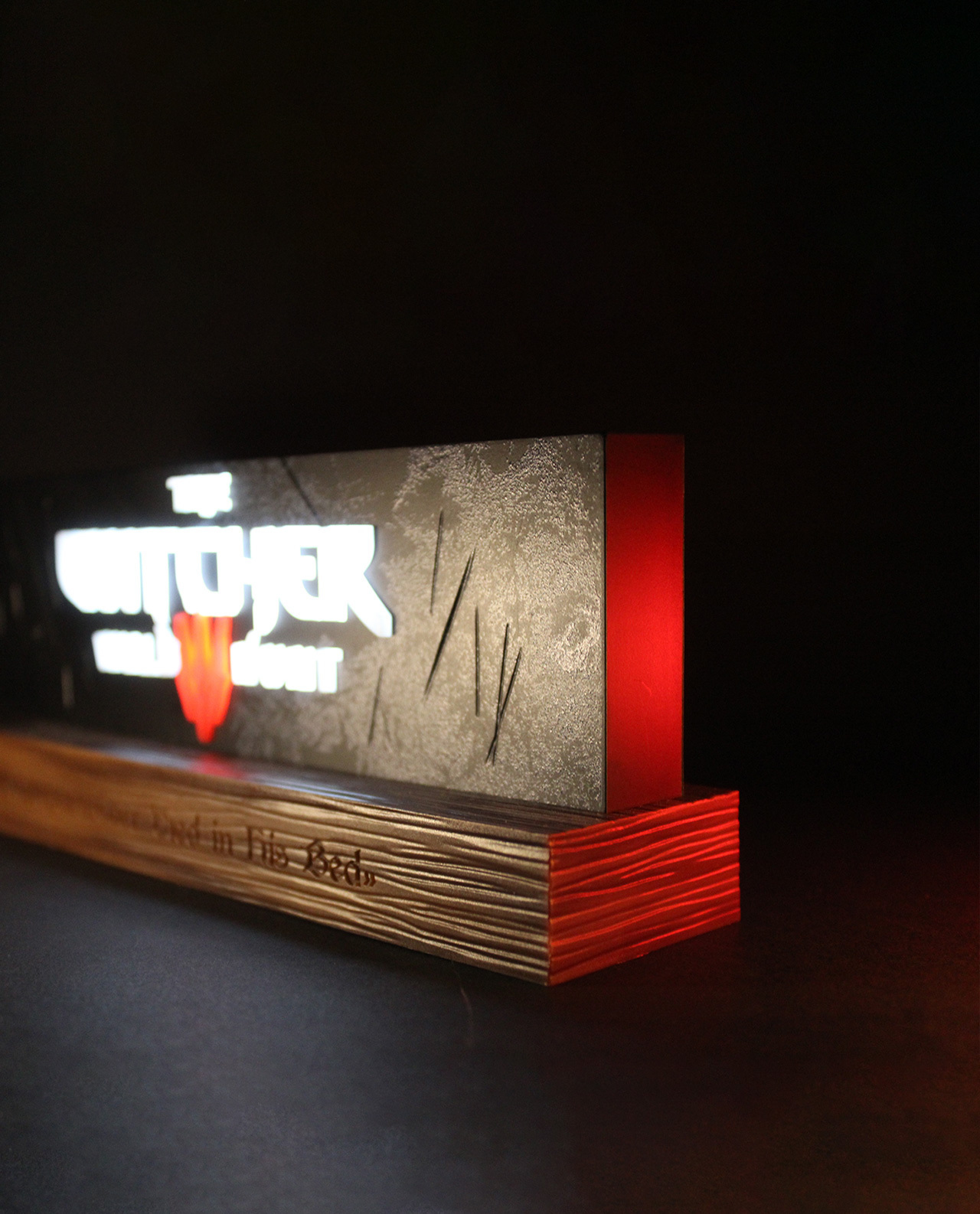 Un cartello di Witcher. Ha un logo, un titolo e alcuni graffi. La base è in legno. Lo sfondo è scuro.