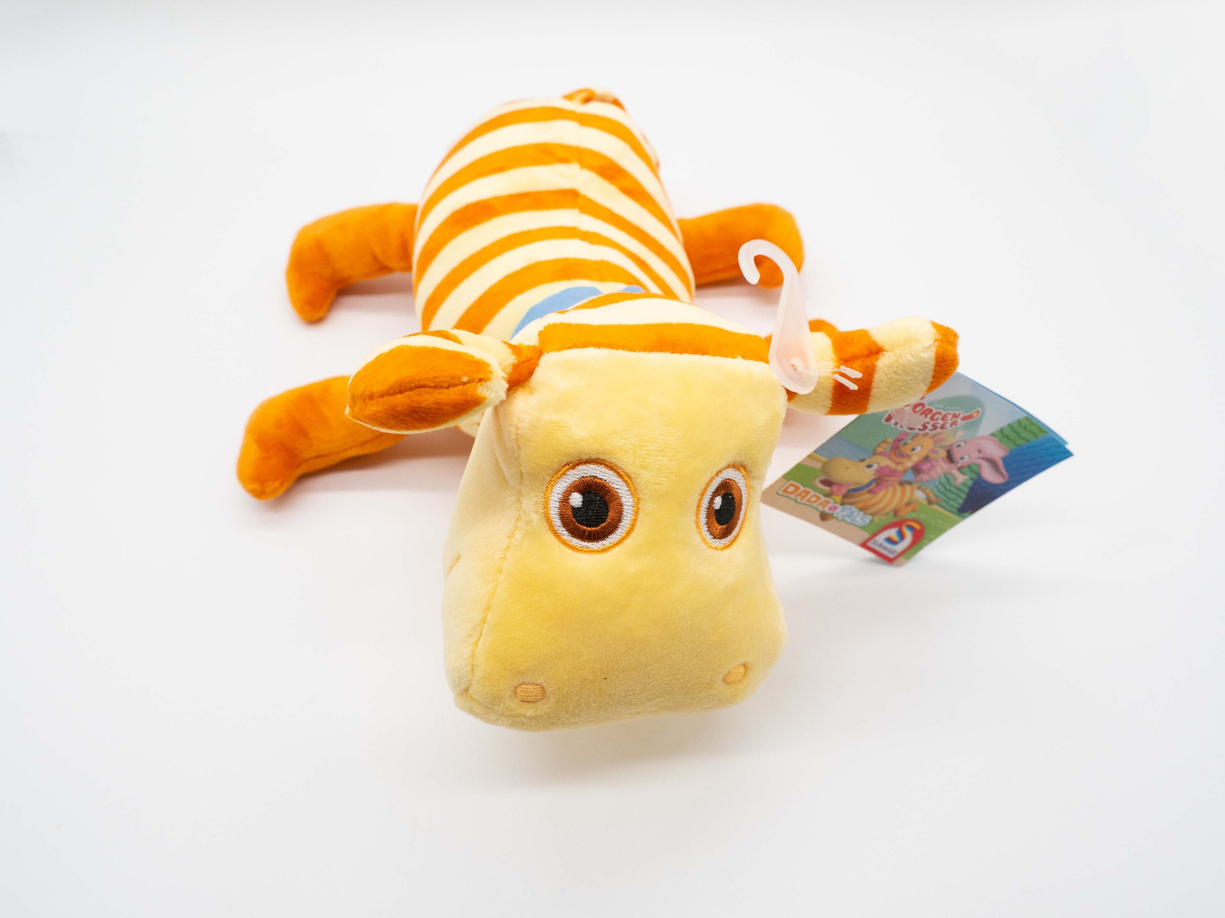 Ein Stofftier-Nilpferd in Gelb und Orange mit einem angebrachten Anhänger. Weißer Hintergrund.