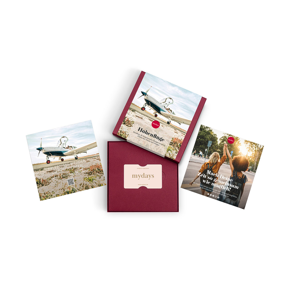 Vier mydays-Geschenkboxen und Flyer auf weißem Grund. Die Flyer zeigen ein Flugzeug, zwei Frauen und eine Geschenkkarte in einer Box mit dem mydays-Logo.