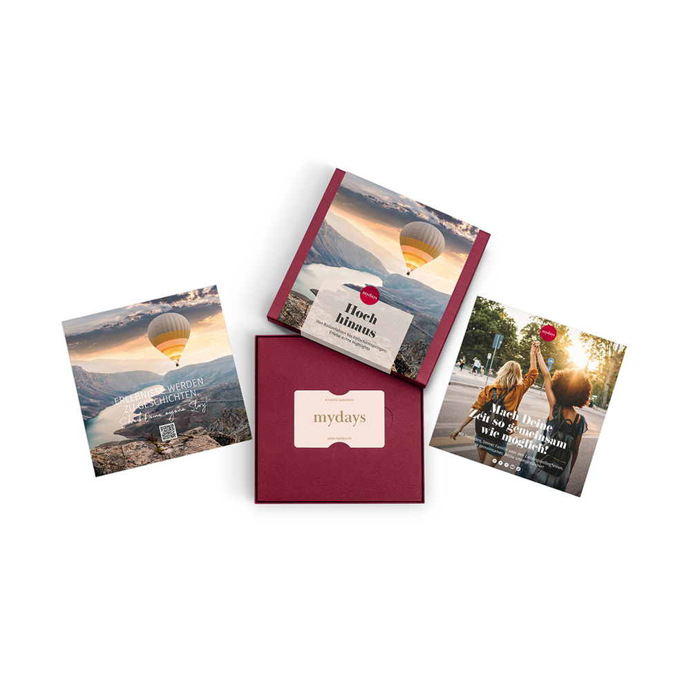 Vier mydays-Werbeartikel. Karten mit Heißluftballonbildern und Personen. Eine rote Box mit einer Geschenkkarte ist ebenfalls vorhanden.