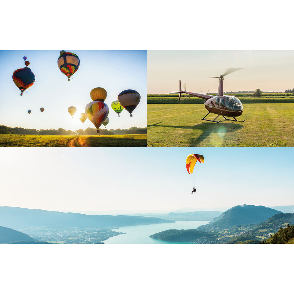Heißluftballons am Himmel, ein Hubschrauber auf Gras und ein Gleitschirmflieger über einem See und Bergen, alles unter blauem Himmel.