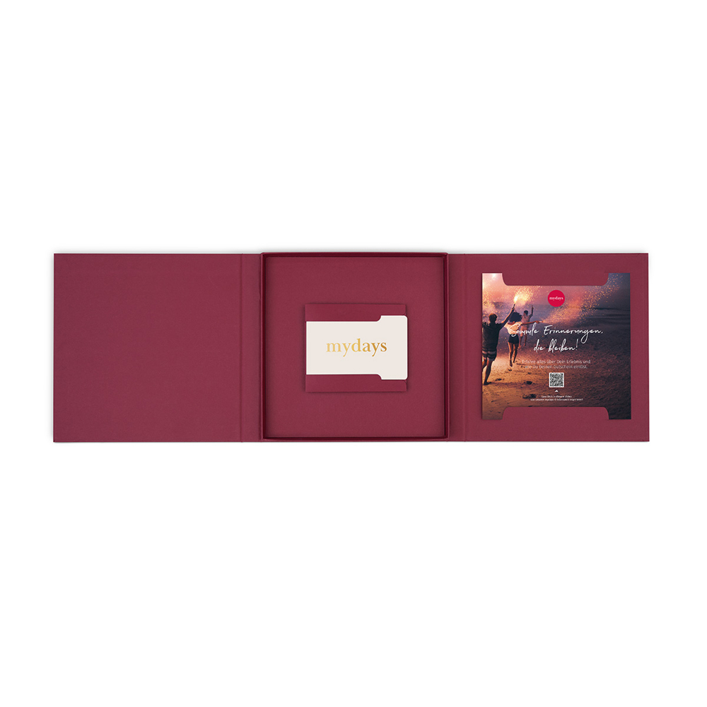 Geöffnete weinrote Geschenkbox mit MyDays-Karte und einem Bild von Menschen mit Wunderkerzen am Strand. Weißer Hintergrund.