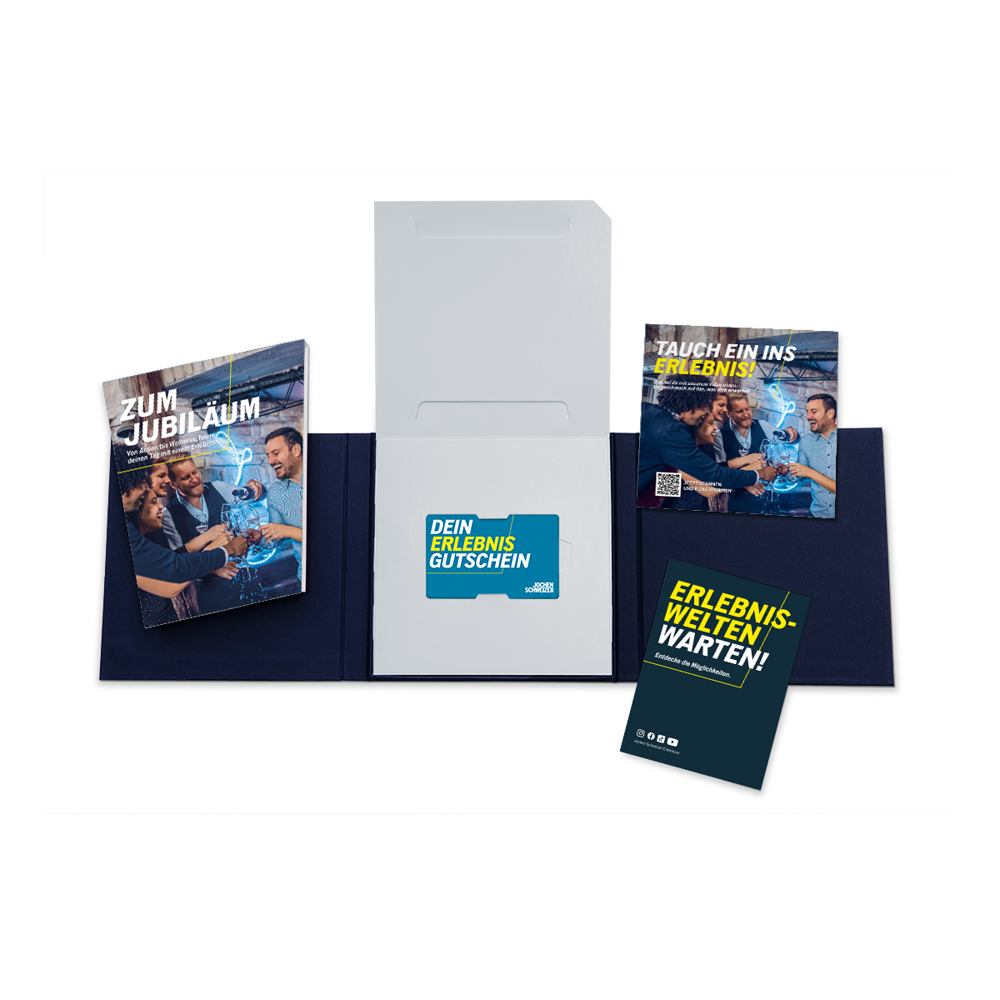Geöffnete Geschenkbox mit Broschüren und einer Geschenkkarte. Die Broschüren enthalten deutschen Text. Die Karte sagt 'DEIN ERLEBNIS GUTSCHEIN'.
