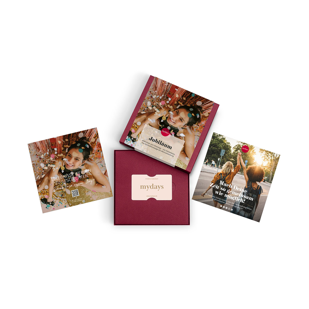 Eine Geschenkbox mit „mydays“-Logo und drei Werbekarten mit Fotos und Text. Konfetti und Personen sind auf den Karten sichtbar.