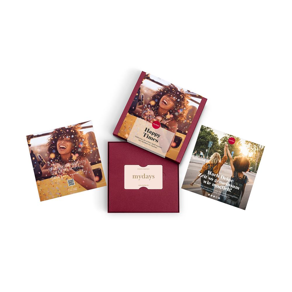 Vier mydays-Werbeartikel. Eine offene Box mit einer Geschenkkarte, drei Flyer mit Bildern von Menschen, die sich amüsieren.