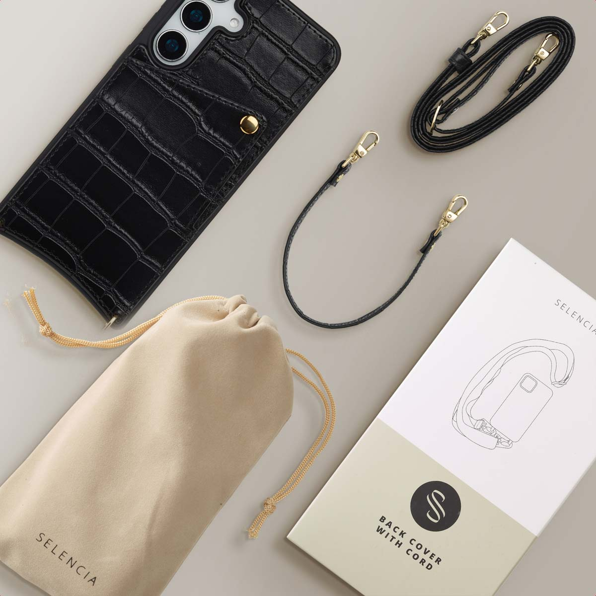 Coque de téléphone noire avec sangle, sac à cordon et boîte de produit sur une surface grise. Tous sont des accessoires pour téléphone.