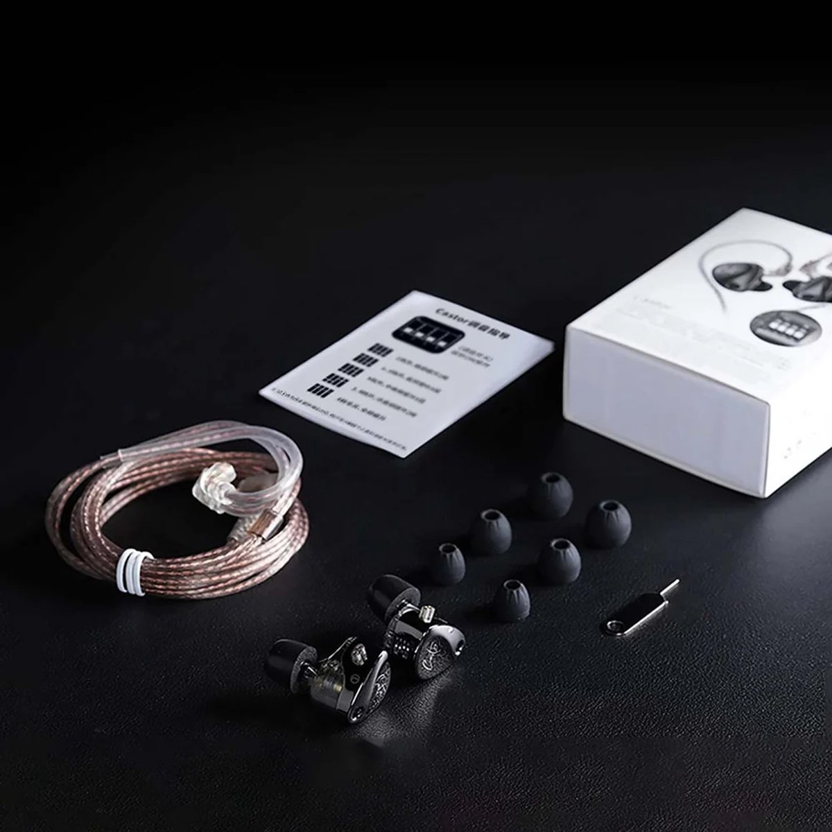 Earphones, cable, ear tips, and box on black surface. The earphones are silver and black. Accessories are present.