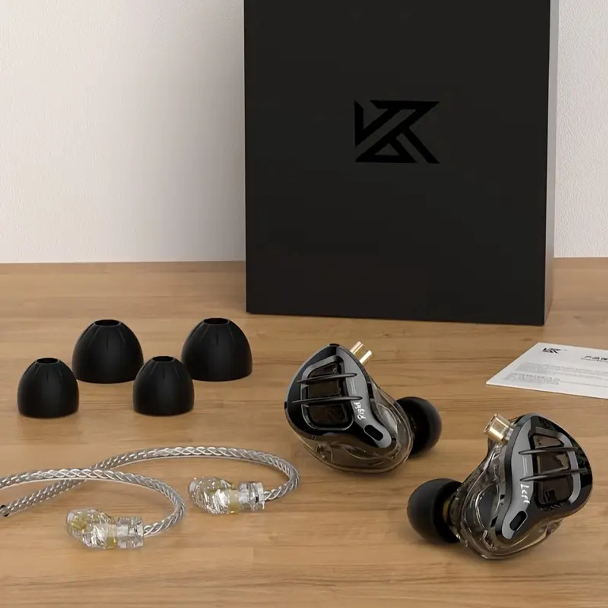 Oortelefoons met extra oortips, een zwarte doos met een logo en een zilveren kabel op een houten oppervlak.