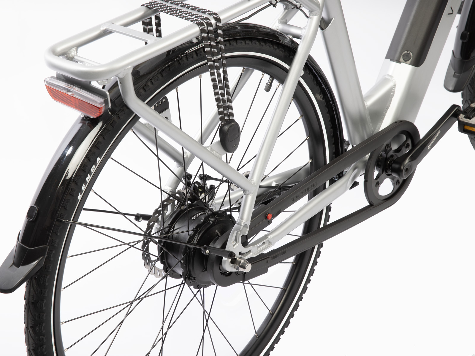 Close-up van een zilveren elektrische fiets. Zichtbare onderdelen zijn het achterwiel, spatbord, bagagerek en ketting. De fiets staat op een witte achtergrond.