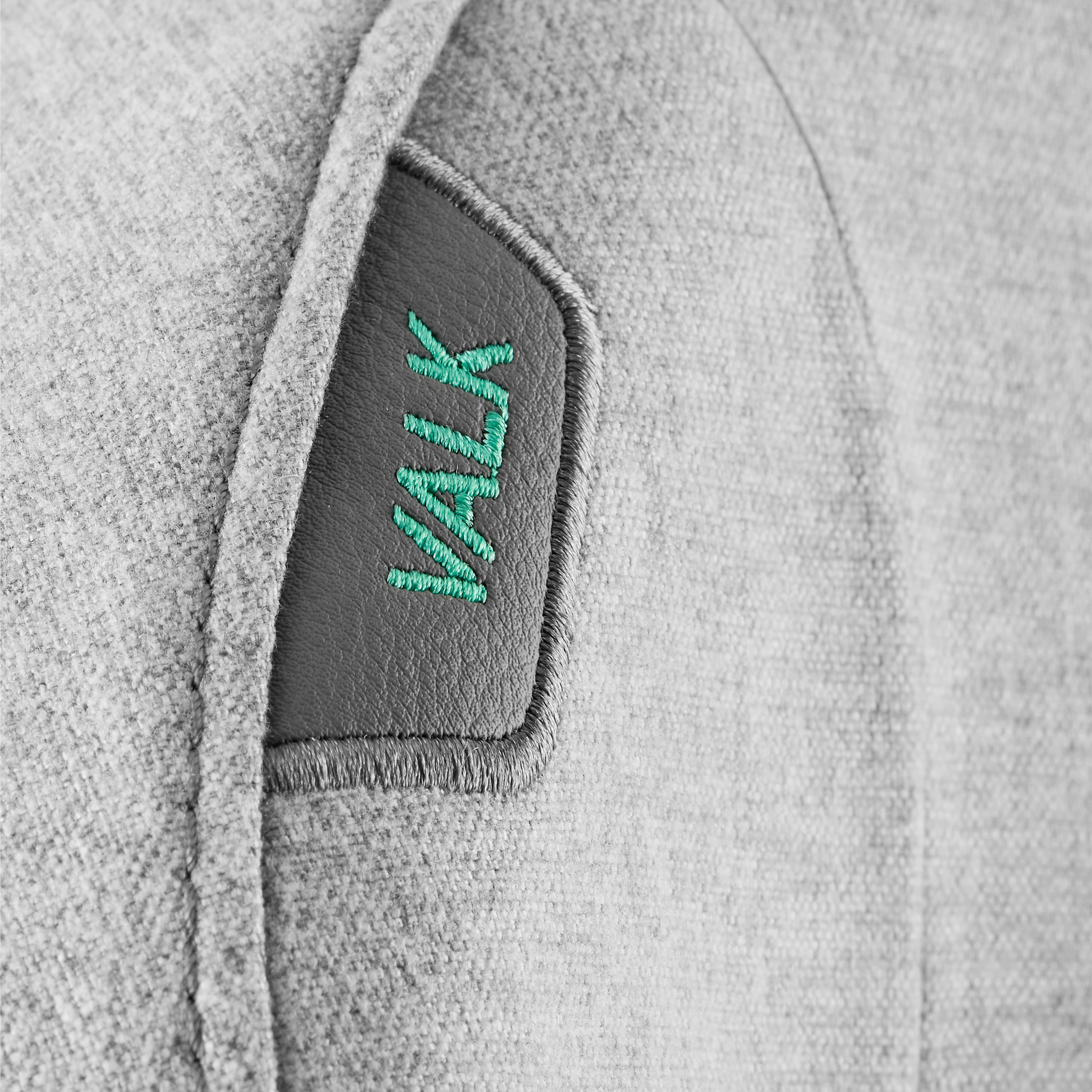 Primer plano de tela gris con un parche de cuero gris oscuro bordado con la palabra VALK en verde.
