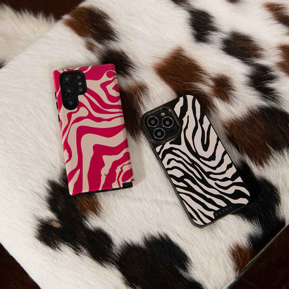 Twee telefoons met zebra- en golvende roze patronen op een oppervlak met koeienvelpatroon.