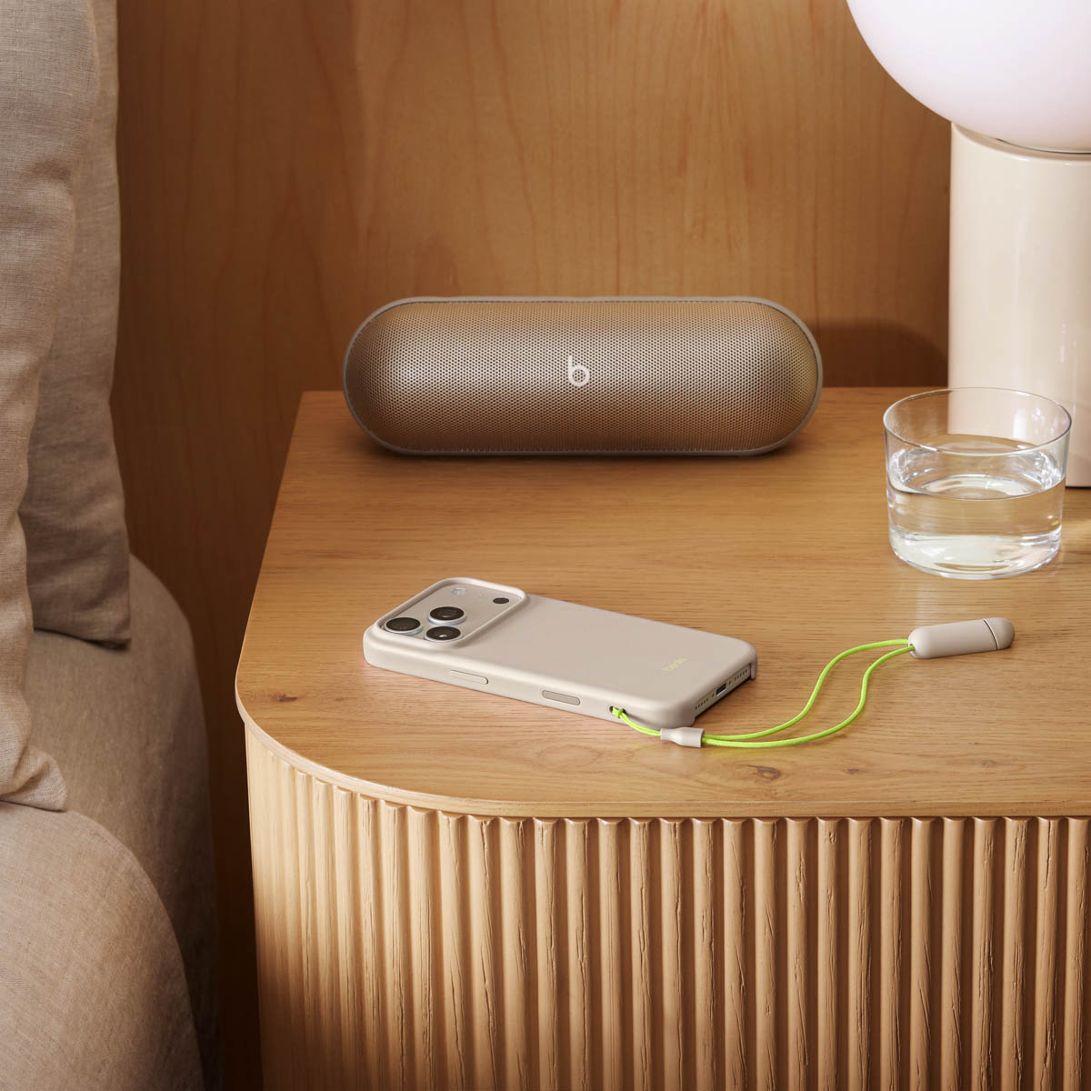 Una mesita de noche con teléfono, altavoz, vaso de agua y lámpara. Un cable verde conecta teléfono y accesorio.