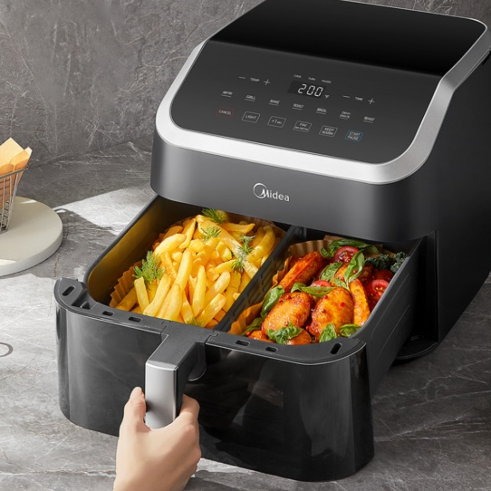Una friggitrice ad aria con patatine fritte e cibo cotto, una persona tiene la maniglia. La friggitrice è su un piano di lavoro grigio.