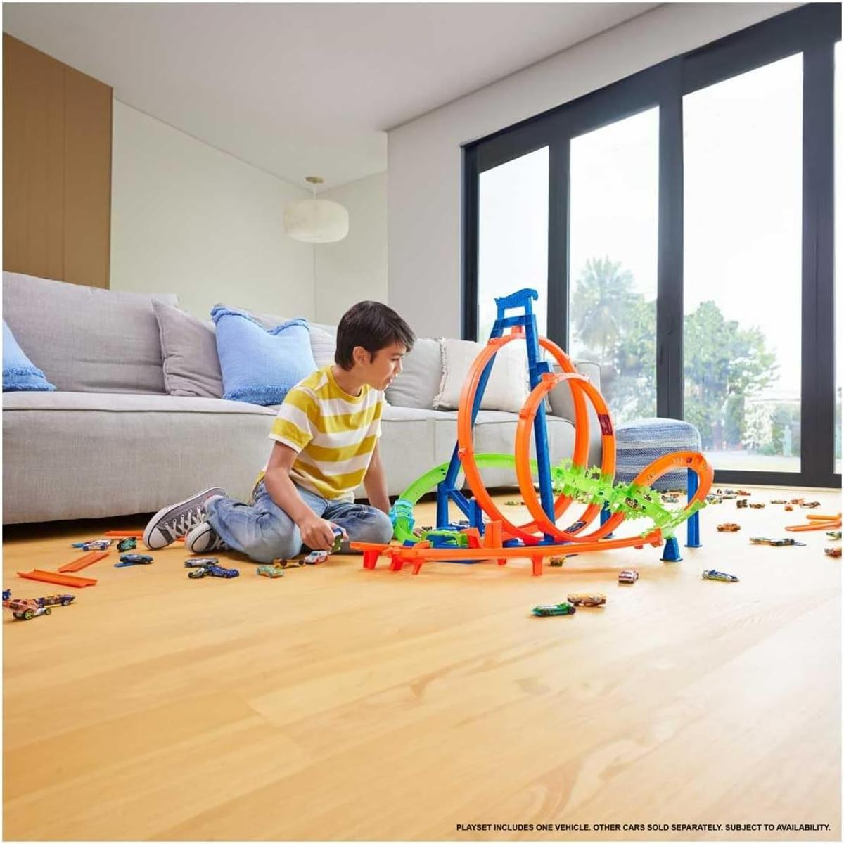 Chłopiec bawi się samochodzikami i torem na drewnianej podłodze. W tle kanapa. Tor ma pętle i skoki.