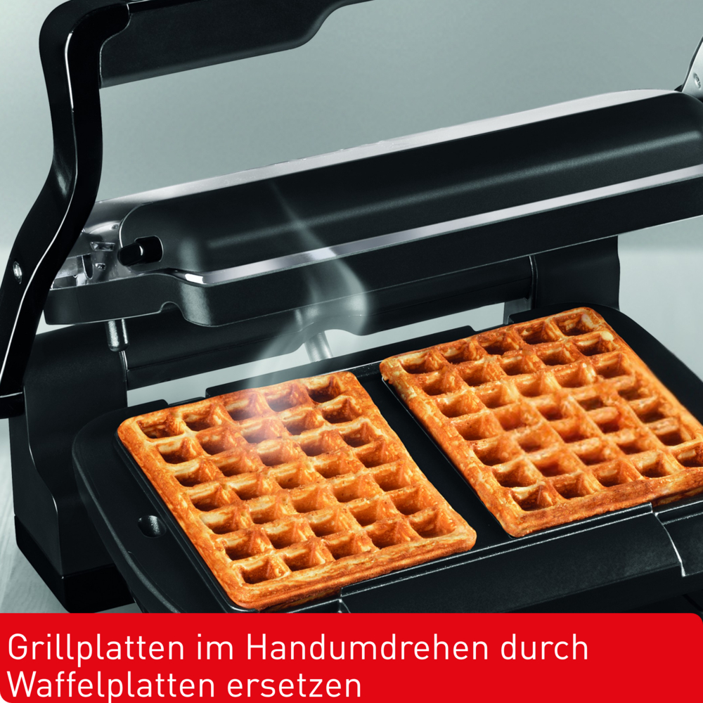 Ein Waffeleisen mit zwei goldenen Waffeln darin. Dampf steigt von den Waffeln auf. Das Eisen ist schwarz und offen.