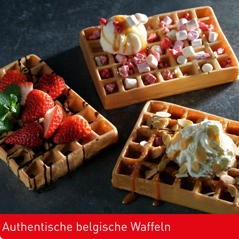 Drei belgische Waffeln mit Belägen: Erdbeeren, Eis, Marshmallows, Schlagsahne und Karamellsauce, auf dunkler Oberfläche.