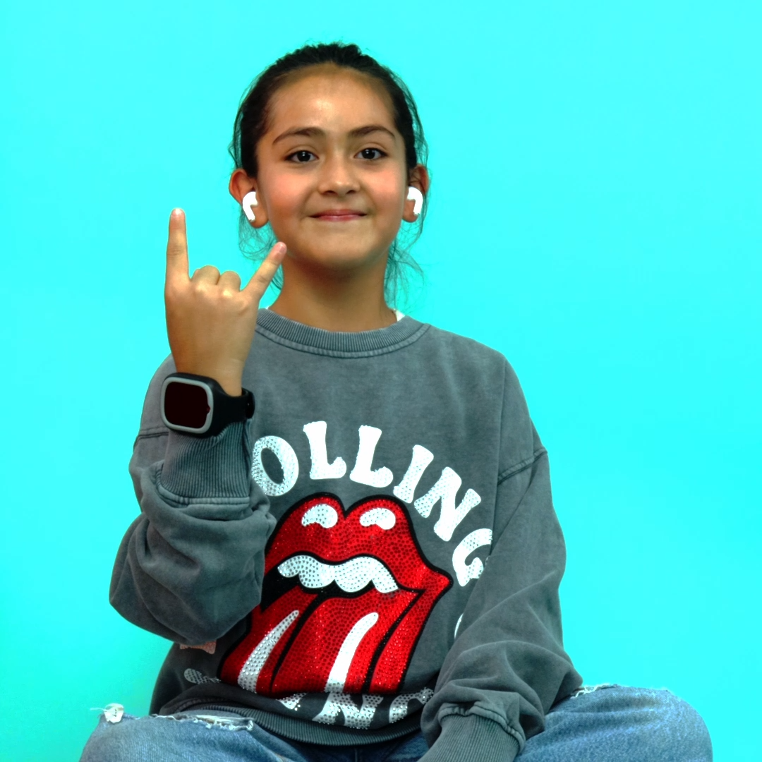 Una niña con auriculares, un reloj y un gesto de rock, con una sudadera de los Rolling Stones. Fondo turquesa.