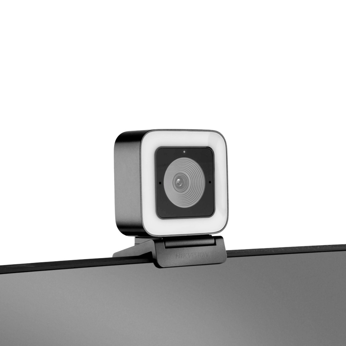 Kamera internetowa o kwadratowym kształcie i jasnym otoczeniu, zamontowana na monitorze. Obiektyw jest pośrodku.