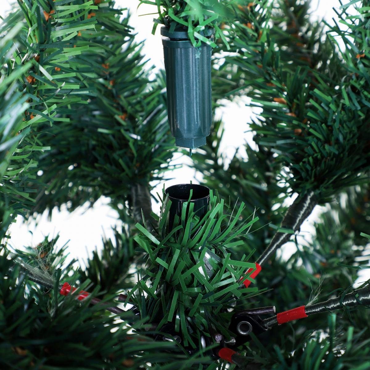 Nahaufnahme eines grünen künstlichen Weihnachtsbaumabschnitts. Ein dunkelgrüner Stecker befindet sich über einer schwarzen Basis. Drähte mit roten Enden sind sichtbar.