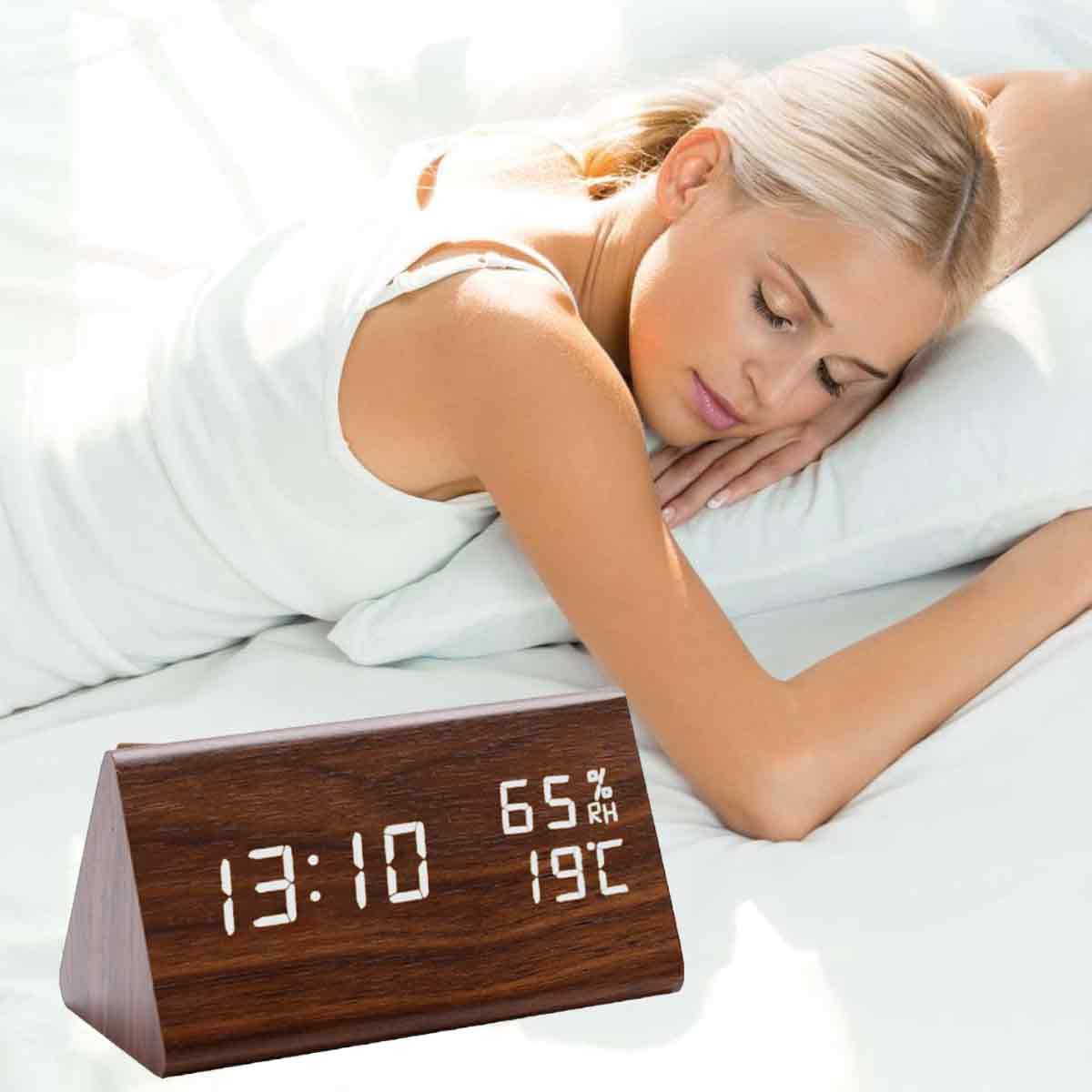 Eine Frau schläft im Bett. Eine digitale Holzuhr zeigt 13:10, 65 % Luftfeuchtigkeit und 19 Grad Celsius an.